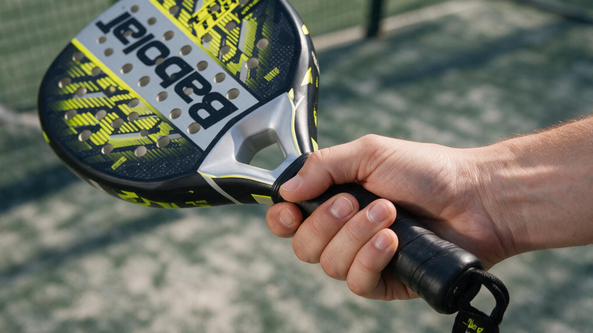 Close-up of a player's hand gripping a Babolat padel racket on a Dubai court